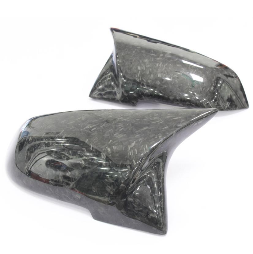 Two dark, carbon fiber car side mirrors rest on a white surface, showcasing a sleek, glossy finish with visible fiber patterns.