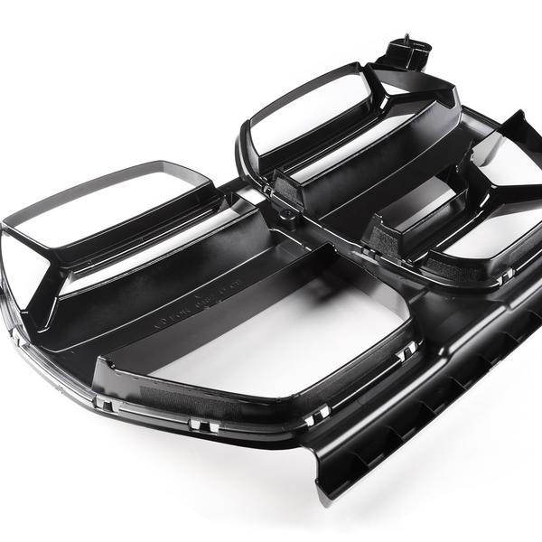 Black plastic automotive grille on a white background, featuring multiple rectangular openings and angular design elements, resting flat with a reflective sheen highlighting its contours.