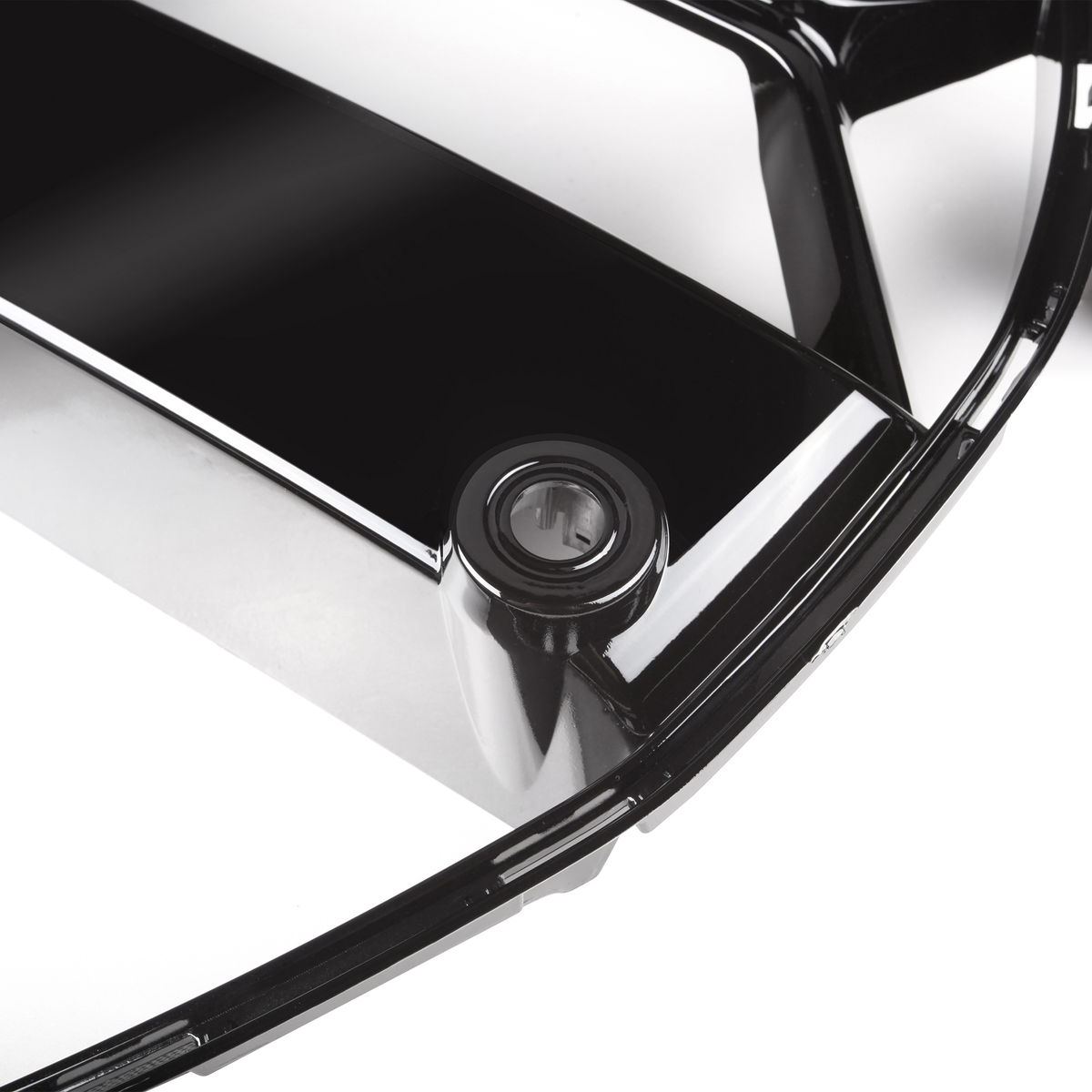 A glossy black plastic car part, possibly a grille, features a circular detail set within it. The surrounding area is a plain white background, highlighting the sheen of the part.