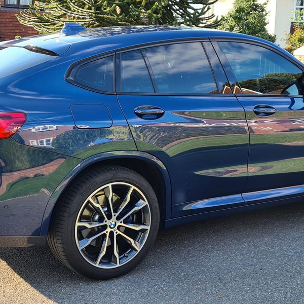 A blue car is parked on a residential street, featuring sleek design and alloy wheels. Brick houses and green foliage surround the scene. The license plate reads "LUMMA ACCENTS."
