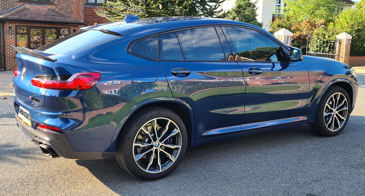 A blue car is parked on a residential street, featuring sleek design and alloy wheels. Brick houses and green foliage surround the scene. The license plate reads "LUMMA ACCENTS."