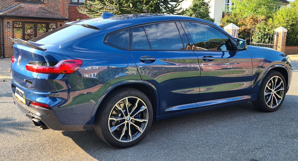 A blue car is parked on a residential street, featuring sleek design and alloy wheels. Brick houses and green foliage surround the scene. The license plate reads "LUMMA ACCENTS."