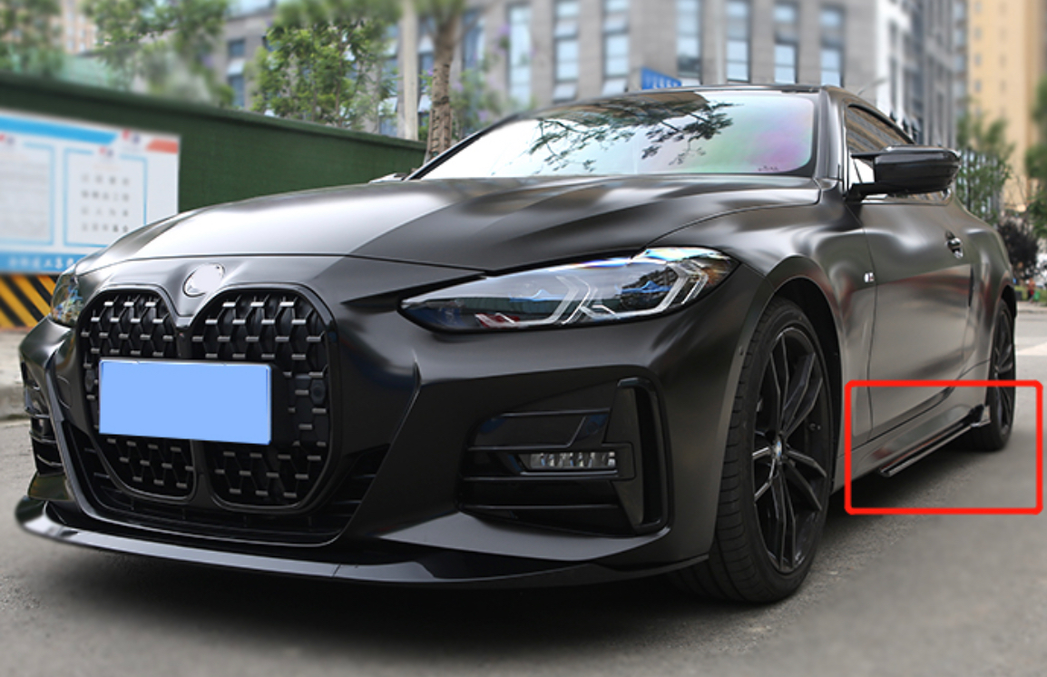A sleek black car is parked on a city street. It has a large grille and modern headlights. A red rectangle highlights a detail near the car's bottom side.