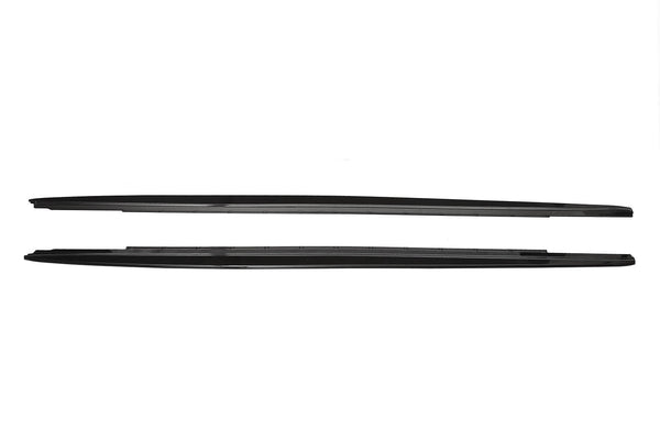 Two sleek, black car side skirts, aligned horizontally, lie against a plain white background, showing their aerodynamic design and smooth edges.