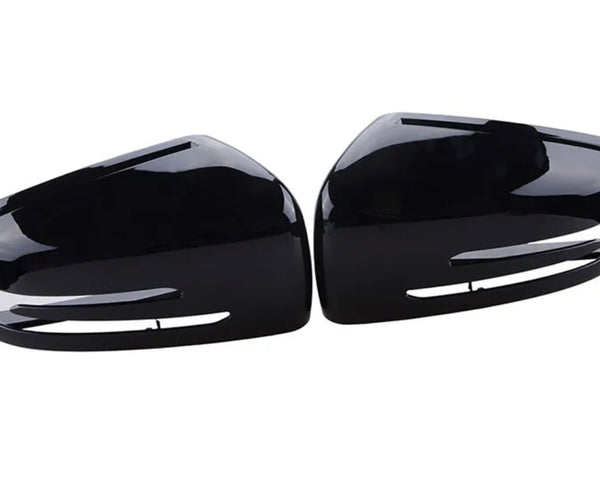 Glossy black car side mirror covers lie face up, displaying their sleek, aerodynamic shape. Positioned parallel to each other, they rest on a white, featureless background.