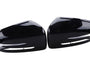 Glossy black car side mirror covers lie face up, displaying their sleek, aerodynamic shape. Positioned parallel to each other, they rest on a white, featureless background.