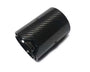 A glossy black carbon fiber exhaust tip lies against a white background, its cylindrical shape adorned with subtle diagonal patterns and screws, featuring an emblem resembling “M” outlined near the edge.