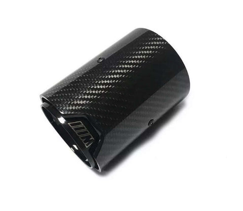 A glossy black carbon fiber exhaust tip lies against a white background, its cylindrical shape adorned with subtle diagonal patterns and screws, featuring an emblem resembling “M” outlined near the edge.