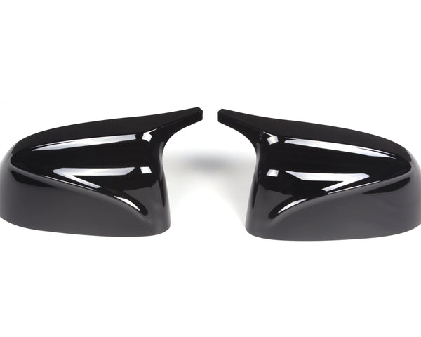 Two glossy black side mirror covers, angled symmetrically, with curved lines, placed on a plain white surface.