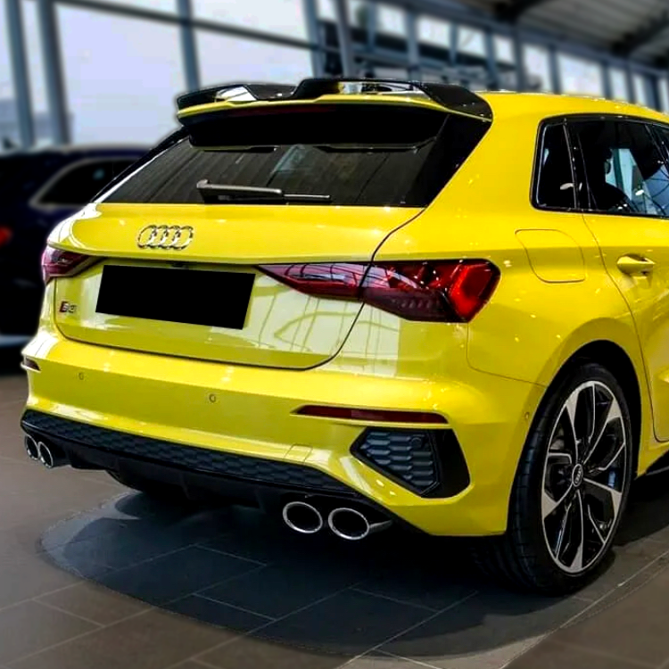 A yellow Audi car is parked in a showroom, showcasing a sporty rear design with dual exhausts under bright lighting. A black license plate covers the rear branding.