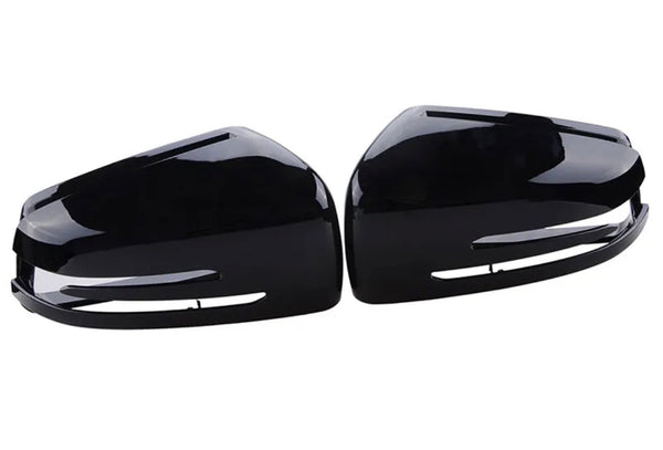 Two sleek, black side mirror covers are positioned side by side, showcasing a glossy surface and streamlined design, set against a plain white background.