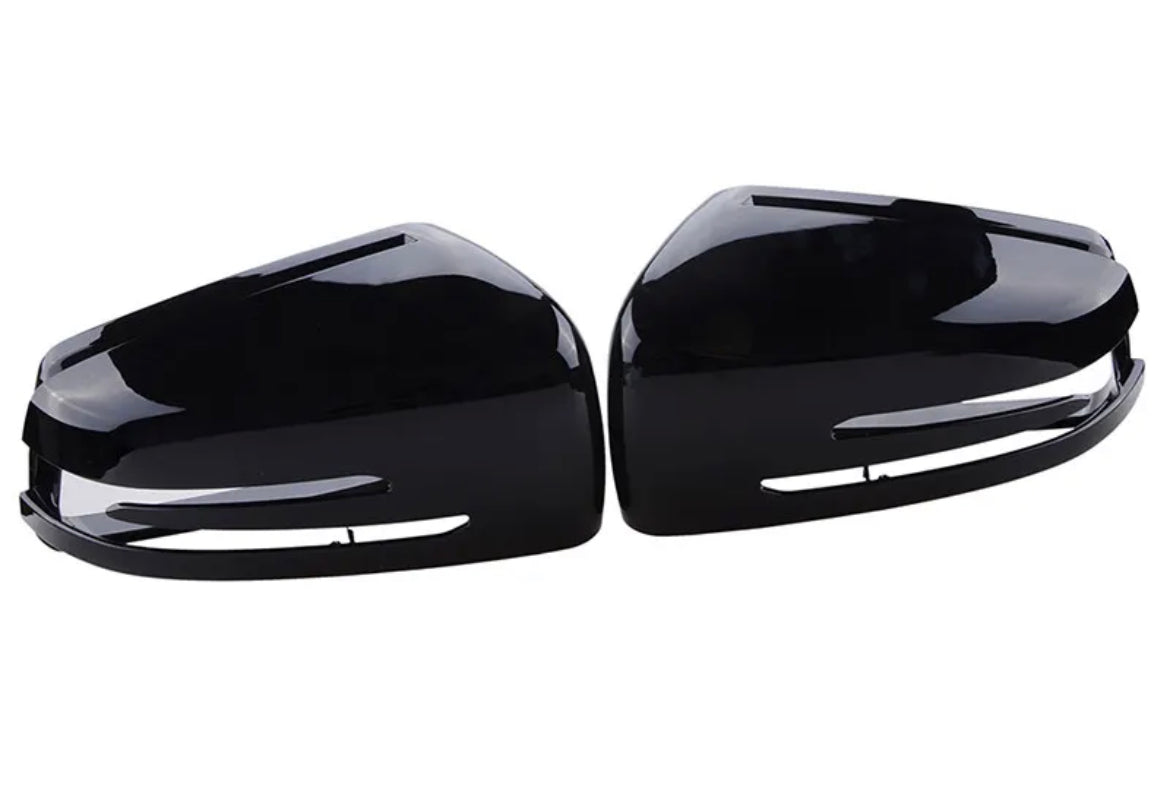 Two shiny black car side mirror covers are placed facing each other against a plain white background. The covers have slits for turn signal lights and a sleek, modern design.
