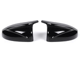 Two sleek black car side mirror covers face each other, reflecting light. They rest on a plain white background, showcasing their glossy finish and aerodynamic design.