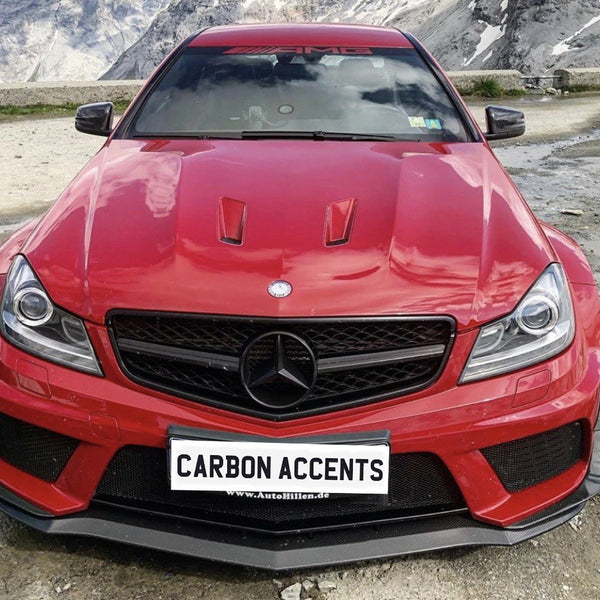 A red Mercedes-Benz car is parked on a mountainous landscape with rocky terrain. The front features "CARBON ACCENTS" and "www.AutoHillen.de" text on the license plate.