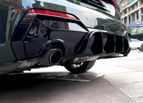 Car exhaust pipe releasing emission, surrounded by a glossy black rear bumper with vents. Reflective cityscape in the metal surface, parked on an urban street.