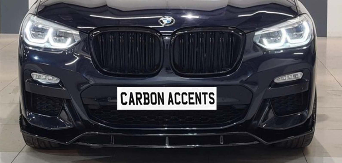 Car front grille with illuminated headlights; BMW logo above, and "CARBON ACCENTS" text on a simulated plate. The car is in a showroom setting with a tiled floor.