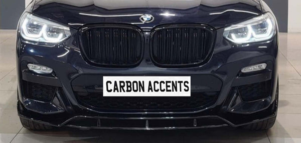 Car front grille with illuminated headlights; BMW logo above, and "CARBON ACCENTS" text on a simulated plate. The car is in a showroom setting with a tiled floor.