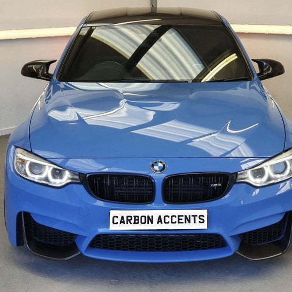 A blue BMW sports car, parked in a well-lit showroom, features the text "CARBON ACCENTS" on the license plate.