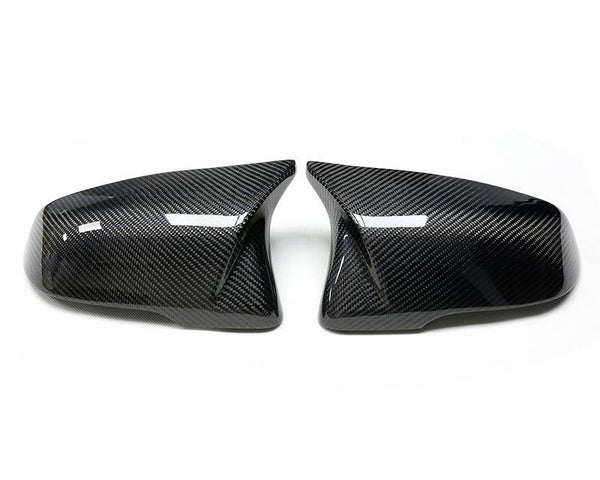 Two carbon fiber car mirror covers, resting side by side, reflect light on a plain white background.