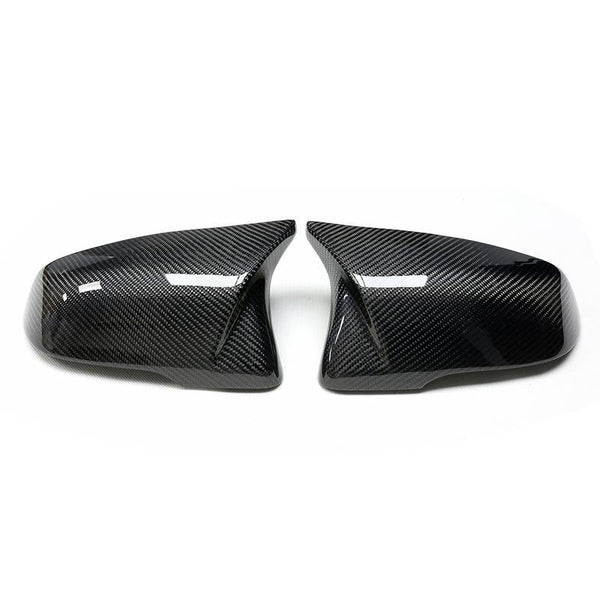 Two carbon fiber car mirror covers, resting side by side, reflect light on a plain white background.