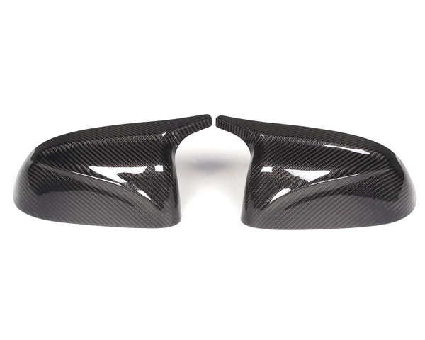 Two carbon fiber car mirror covers are placed side by side, angled inward, on a plain white background. The glossy surface reflects light, highlighting their textured pattern.