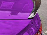 A vibrant purple car with a carbon fiber spoiler is parked, reflecting building windows on its glossy surface. Tail lights are partially visible, hinting at a rear view.