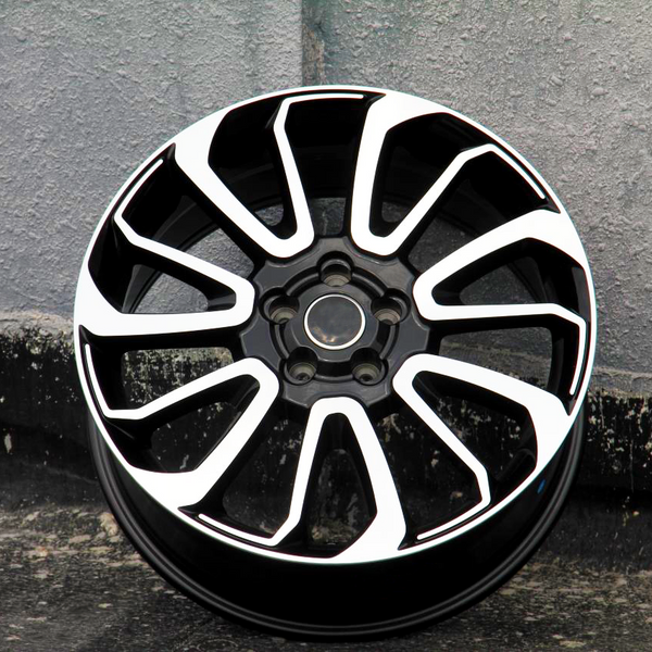 A black alloy wheel with white accents lies against a textured concrete wall, showcasing a sleek, geometric design with multiple spokes.