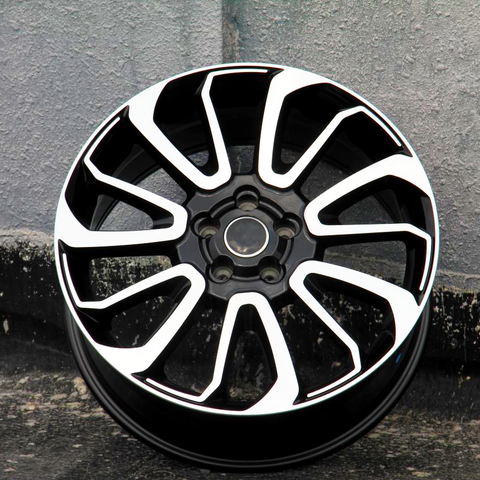 A black alloy wheel with white accents lies against a textured concrete wall, showcasing a sleek, geometric design with multiple spokes.