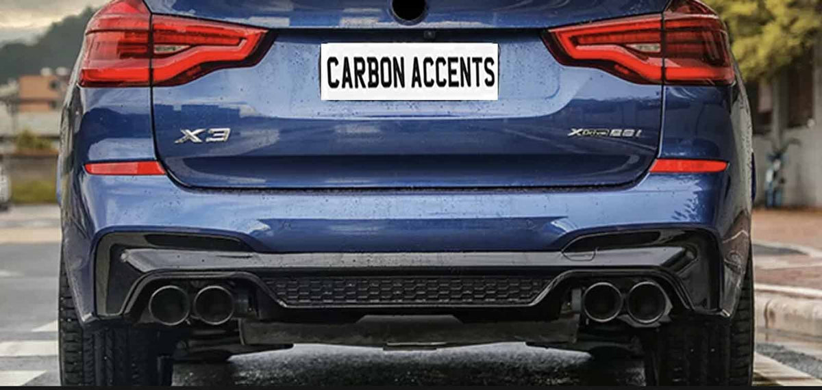 A blue car with dual exhaust pipes is parked on a street. Its license plate reads "CARBON ACCENTS." The surroundings include trees and residential buildings.