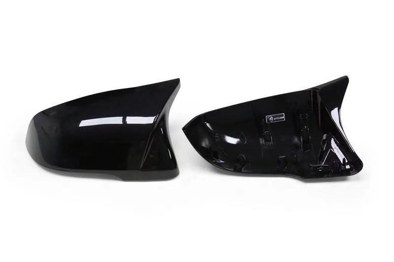 Two glossy black car mirror covers are displayed on a plain white background. One cover is shown from the back, revealing attachment points and a small logo.
