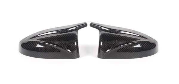 Two carbon fiber side mirror covers rest on a white surface, showcasing a glossy finish and intricate weave pattern, appearing symmetrically aligned.