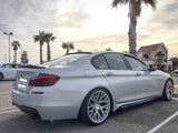 A silver car with custom rims is parked in a lot next to a palm tree. The sky is overcast, and a building is visible in the background.
