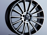 A glossy, black and chrome alloy wheel rests on a pedestal, featuring a three-pointed star emblem at its center, set against a neutral gray background.