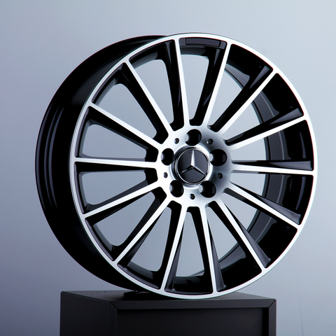 A glossy, black and chrome alloy wheel rests on a pedestal, featuring a three-pointed star emblem at its center, set against a neutral gray background.