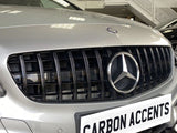 The silver car grille displays a prominent three-pointed logo, surrounded by vertical black slats in a showroom. Below, a white license plate reads 