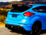 A vibrant blue sports car is parked on a roadside, featuring dual exhausts and a prominent spoiler, with scenic hills and a clear blue sky in the background.