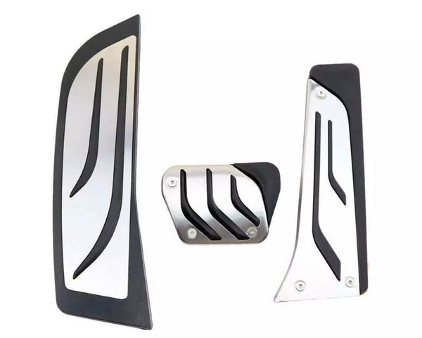 Three metallic car pedals with black rubber grips, featuring diagonal grooves, are arranged against a plain white background.