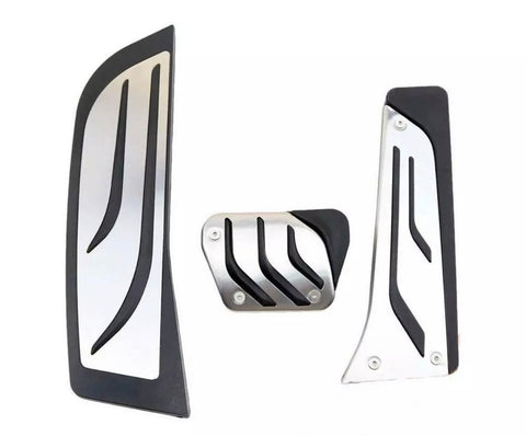Three metallic car pedals with black rubber grips, featuring diagonal grooves, are arranged against a plain white background.