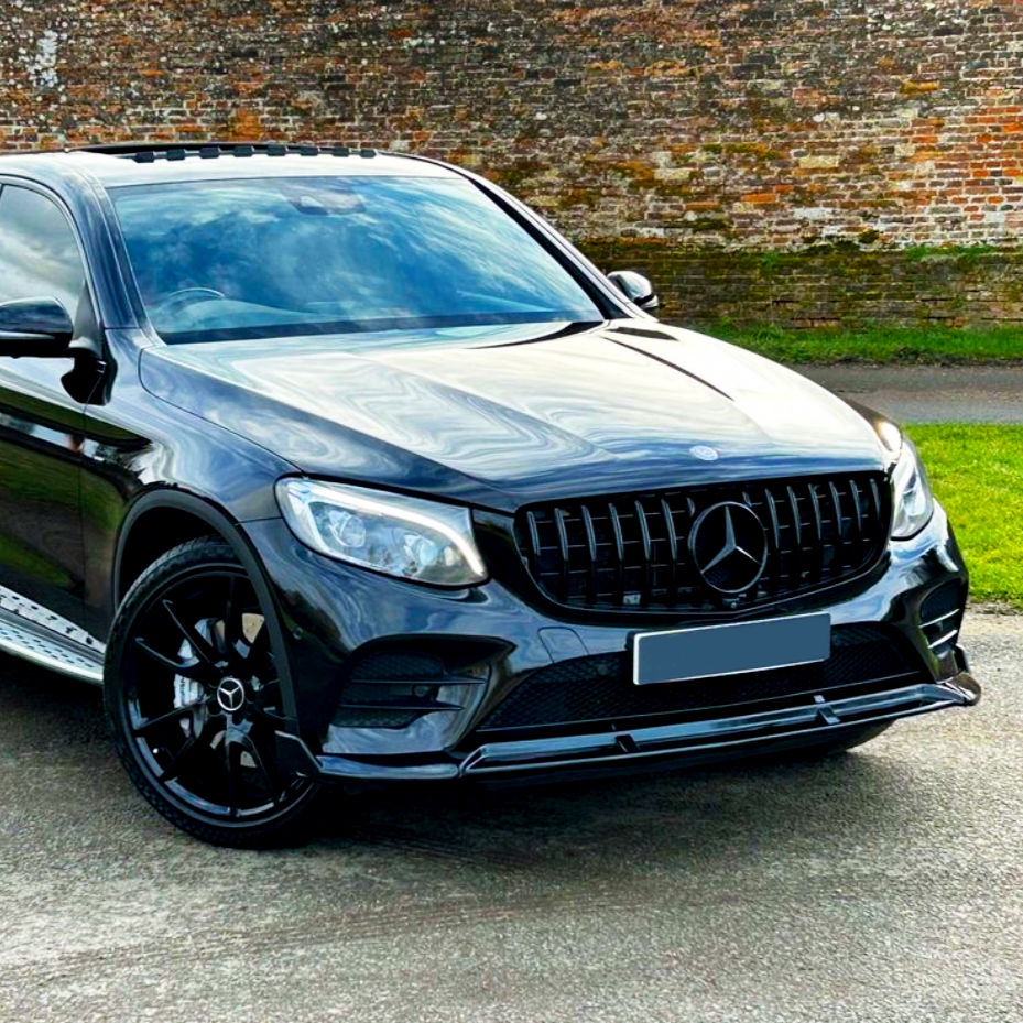 A sleek black SUV with a prominent Mercedes-Benz logo on the grille is parked on a road, set against a backdrop of a brick wall and grass.