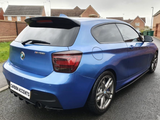 A blue BMW M135i is parked on a wet street, with a 