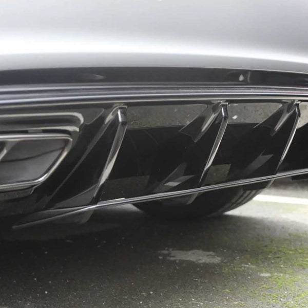 The image features a car's rear diffuser with fin-like protrusions, enhancing aerodynamics. It is parked on an asphalt surface, visible in the background.