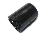 A carbon fiber exhaust tip lies angled on a white background, featuring a glossy checkered pattern with the letter 