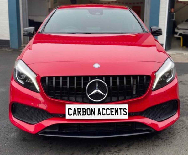 A red car featuring a prominent front grille and sleek headlights is parked outside a garage. The license plate reads "CARBON ACCENTS."