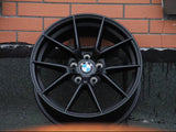 A black BMW wheel rim leans against a brick wall, with 