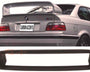 A silver car's rear with a large spoiler and "CARBON ACCENTS" text on the license plate. Below, a detached black car part is displayed in front of a white backdrop.