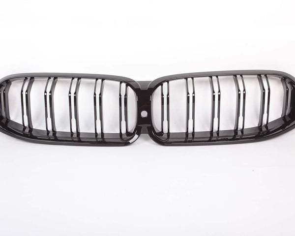 A glossy black car grille with vertical slats, designed in a double kidney shape, is placed against a plain white background.