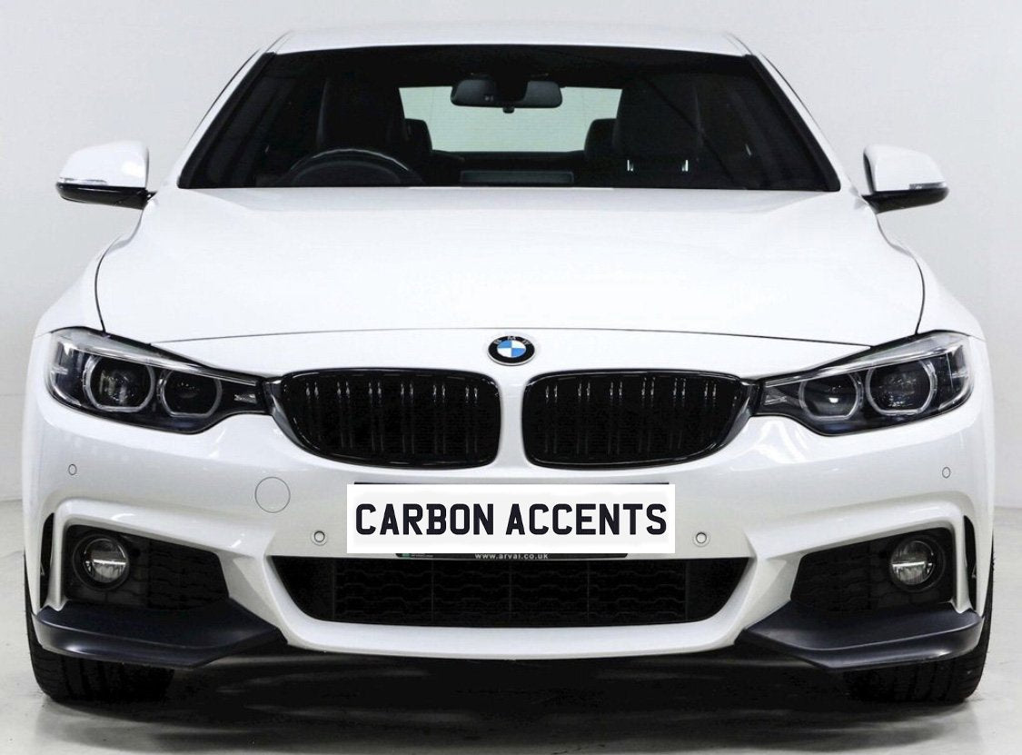 A white BMW car is parked in a studio setting, displaying a front grille and headlights. The license plate reads "CARBON ACCENTS."