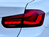 A car's right rear taillight is illuminated red, indicating its stop or parked status, attached to a sleek, white vehicle body with smooth contours and defined lines.