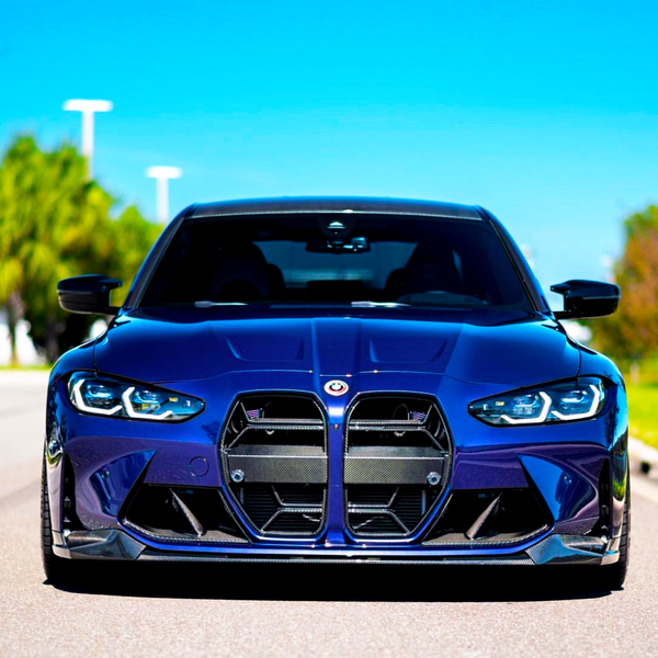 A blue sports car is parked on an empty road, showcasing its aggressive front grille and headlights. The sunny day highlights the car's sleek design, with trees in the background.