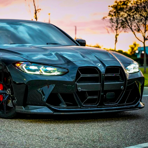 A sleek black car with illuminated headlights is parked on a road at sunset, flanked by trees and a soft pink sky, enhancing the scene's dramatic atmosphere.